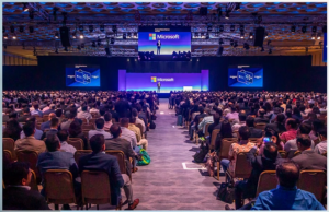 a packed auditorium with a long aisle leading up to a stage with screens