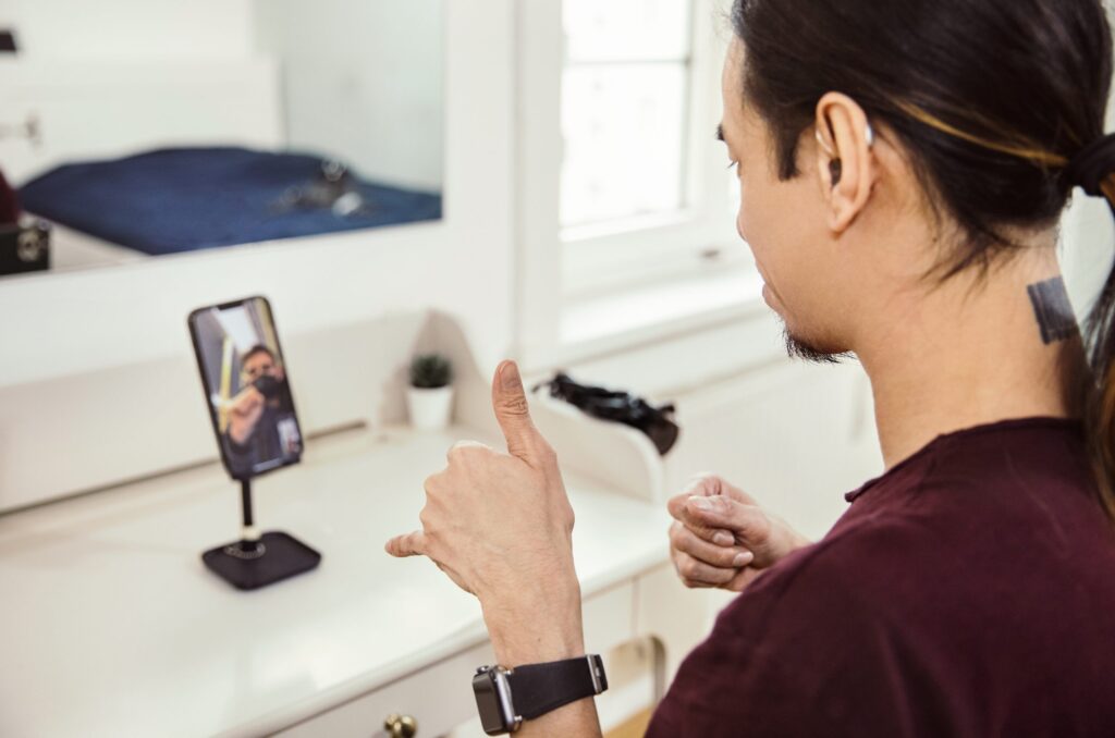 Man signing to person on video call. He has dark hair and is wearing a maroon shirt.