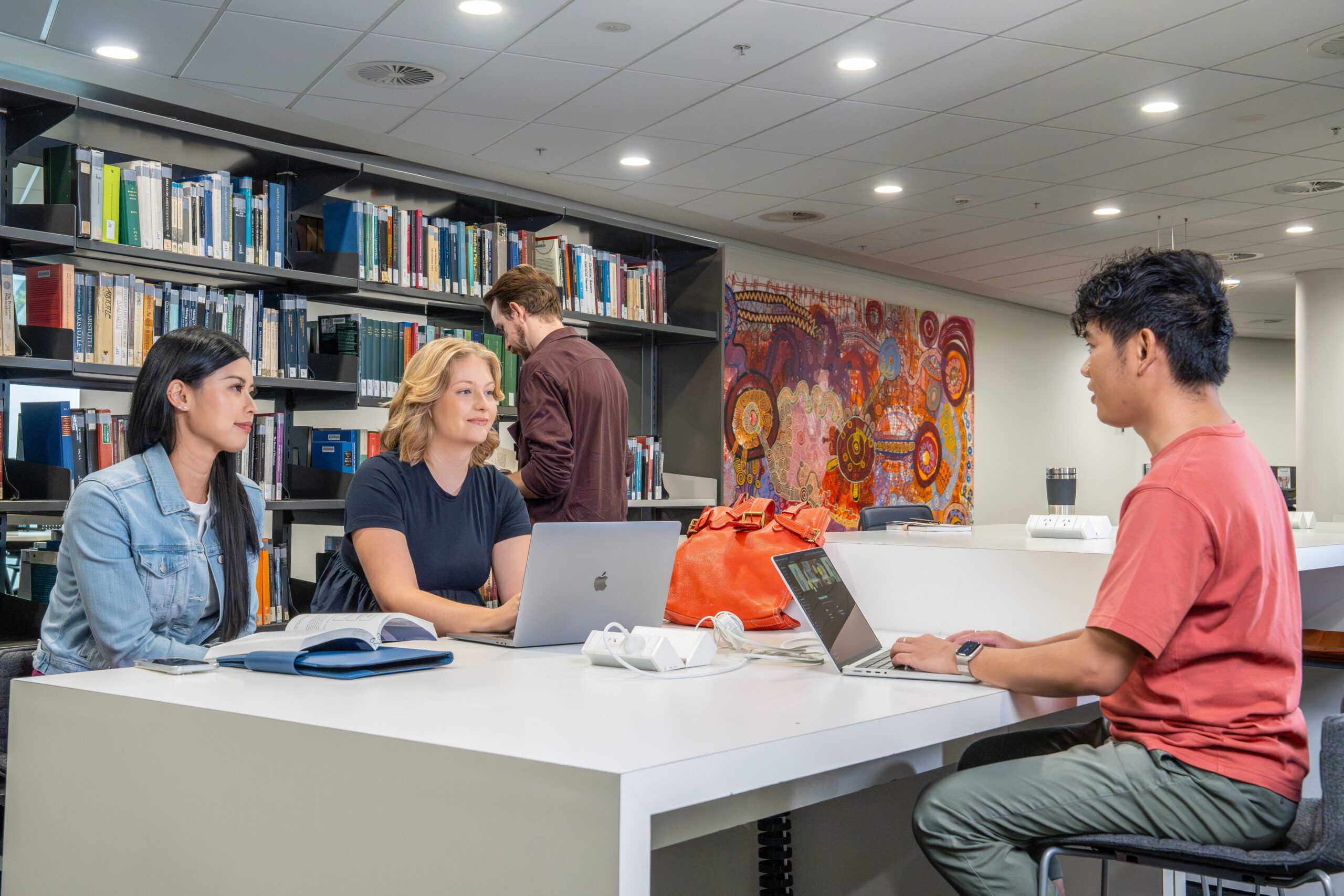 Students sitting around a table in library with laptops