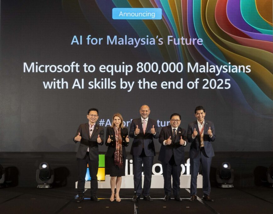 A group of five individuals stands on a stage in front of a large screen displaying the announcement